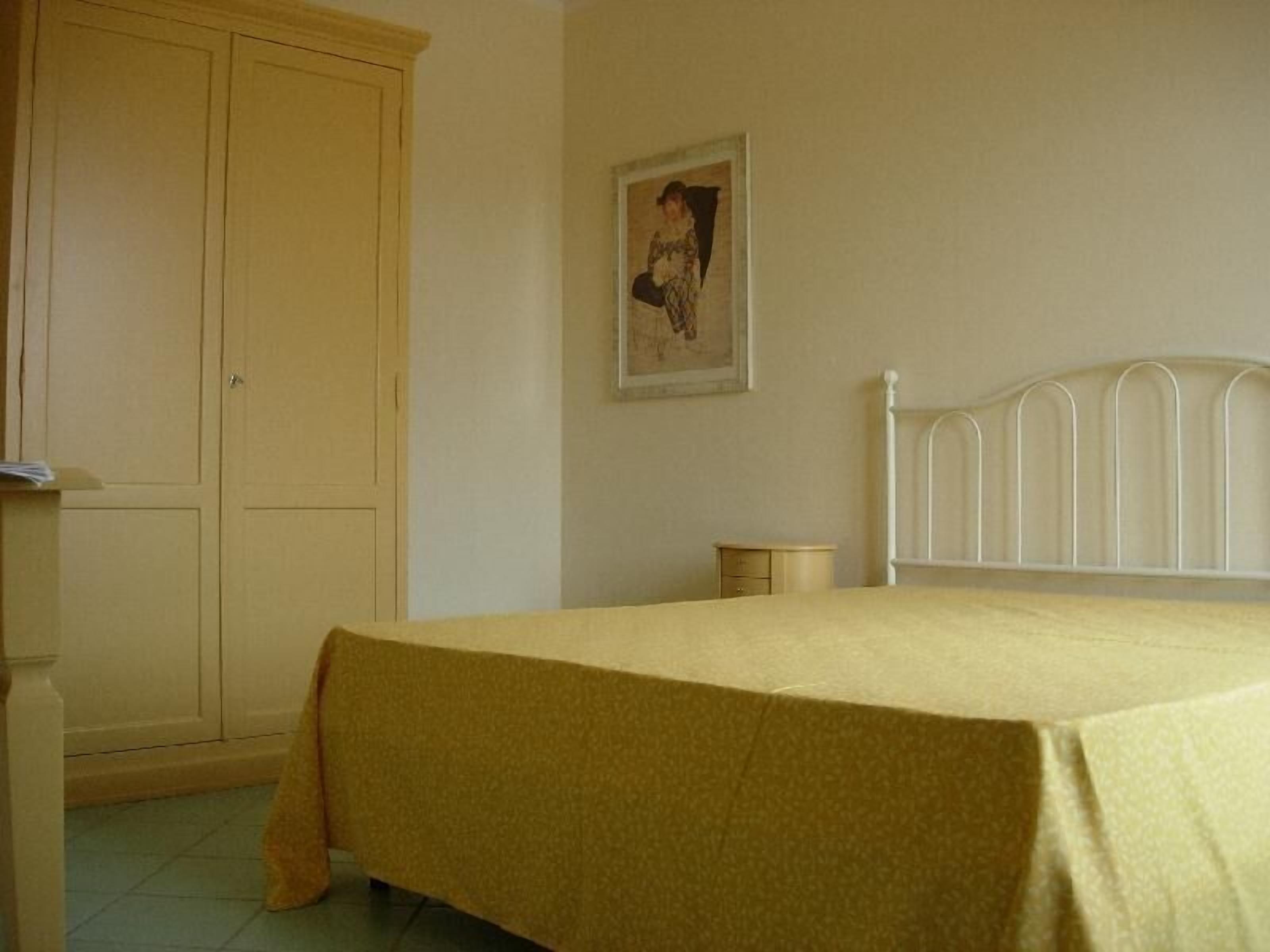 Een slaapkamer met een bed, een kledingkast, een nachtkastje en een aan de muur hangend schilderij.