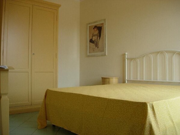 A bedroom with a bed, a wardrobe, a nightstand, and a wall-mounted picture. - Villaggio Turistico Airone (Piombino)