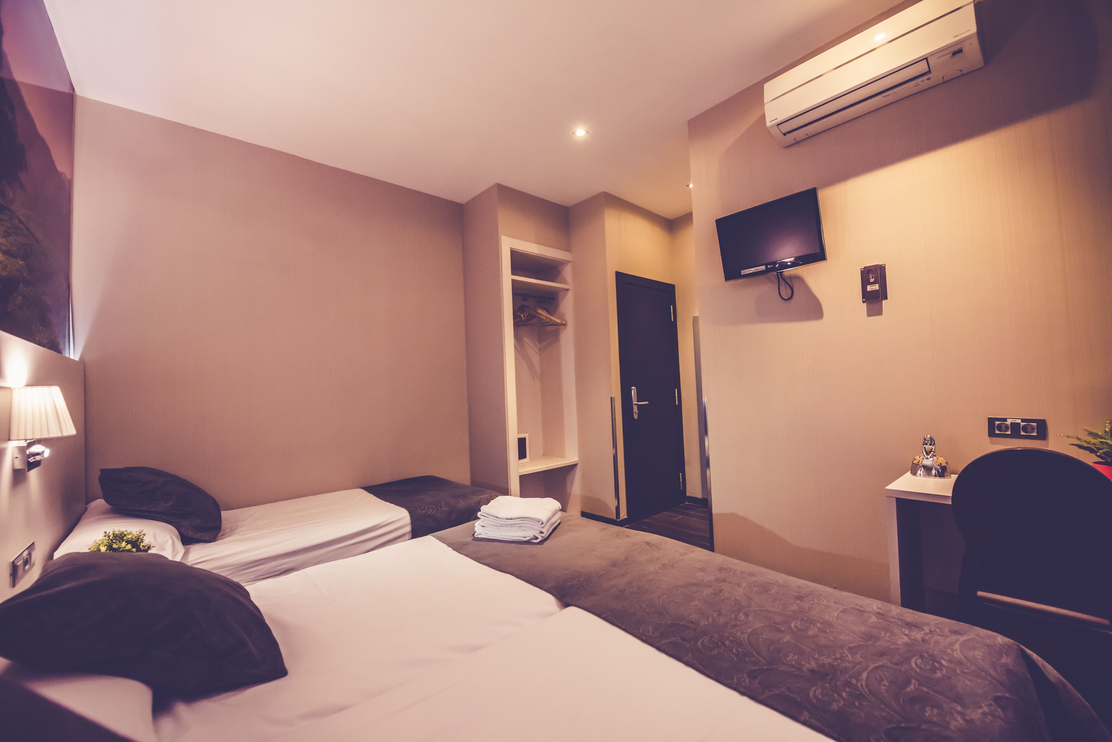 A hotel room with two beds, a wardrobe, a television, and an air conditioning unit.