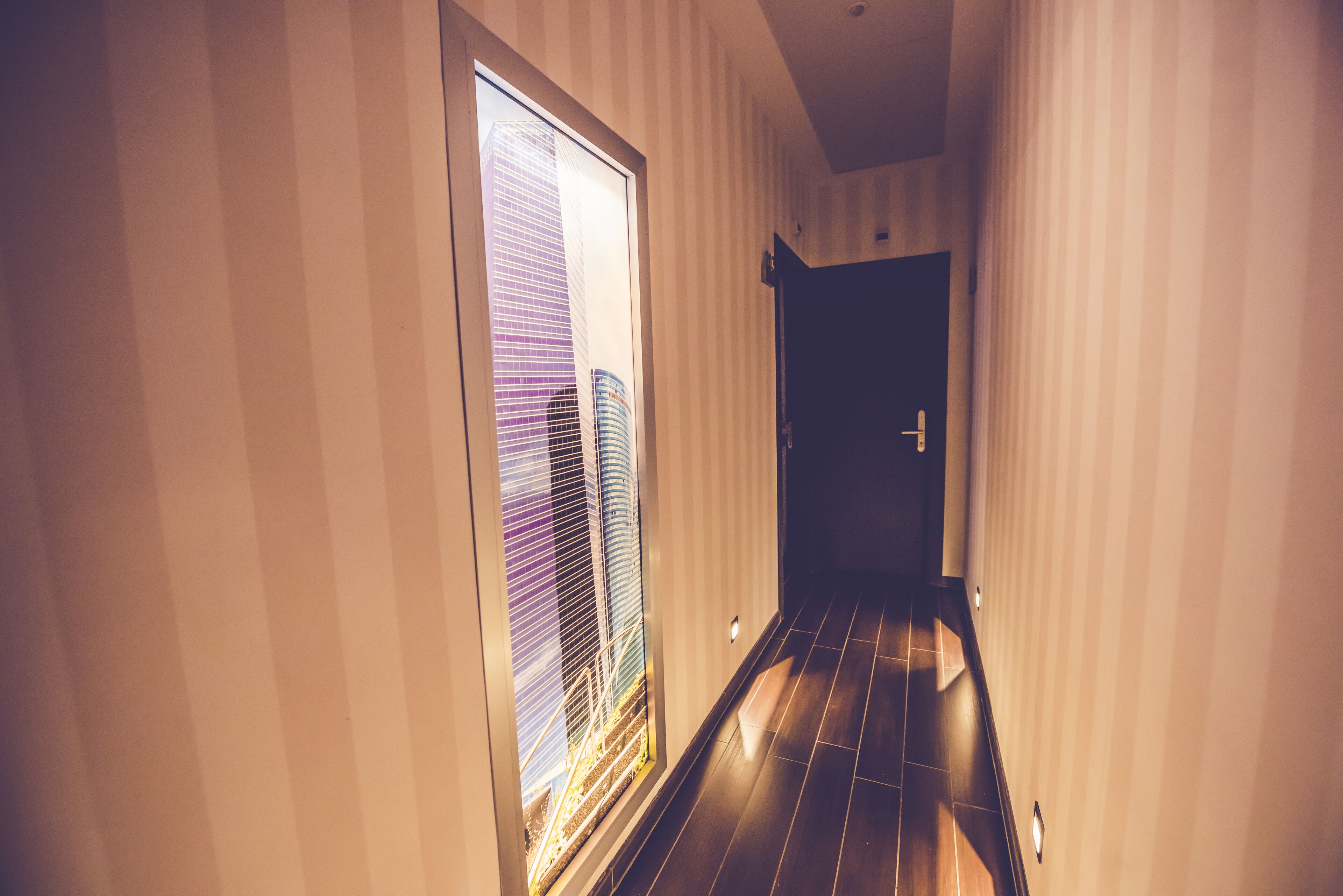 A hallway with striped walls and a wooden floor, leading to a door.