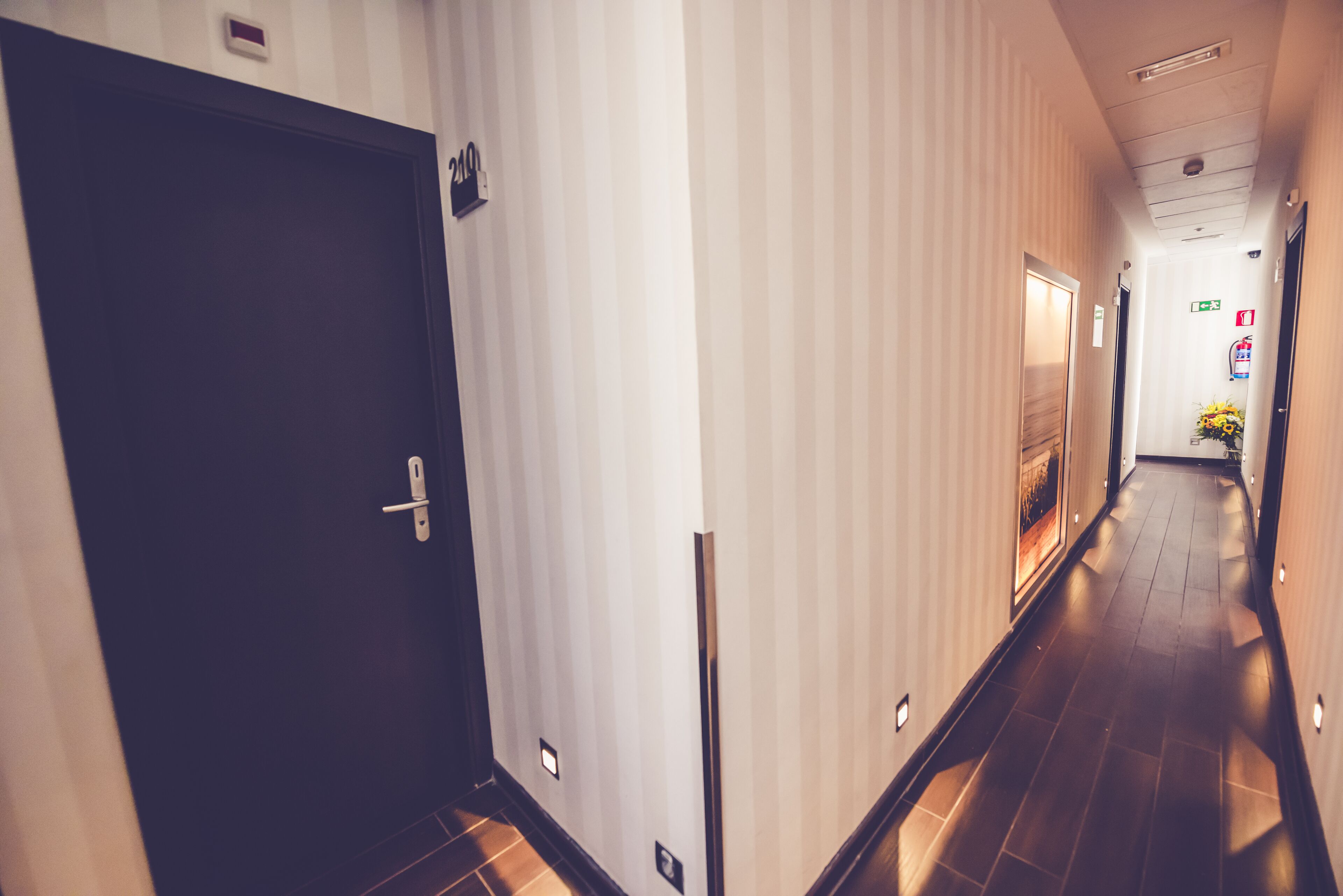 A hotel hallway with a dark door, striped walls, and a tiled floor.