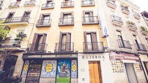 A building with multiple storefronts, including a restaurant named 'Vinos Casa Mon' and a bar named 'H. Lisboa'. - Hostal Prado (Madrid)