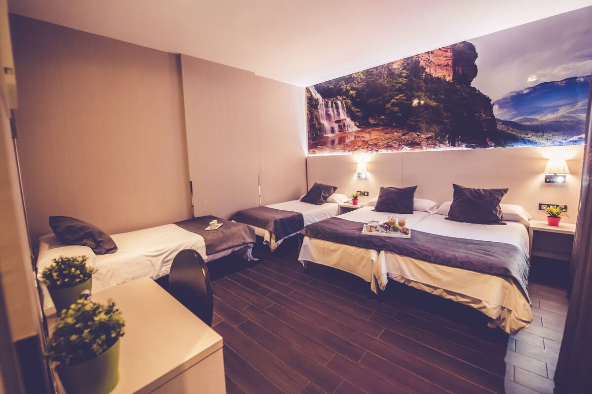 A hotel room with two single beds, a desk, and a large mural of a waterfall.