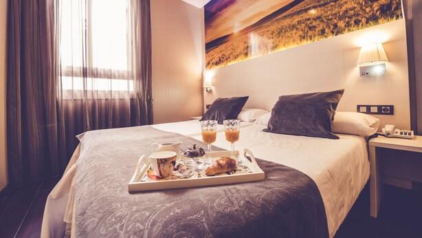 A hotel room with a bed, a tray with breakfast items, a nightstand, and a painting on the wall. - Hostal Prado (Madrid)