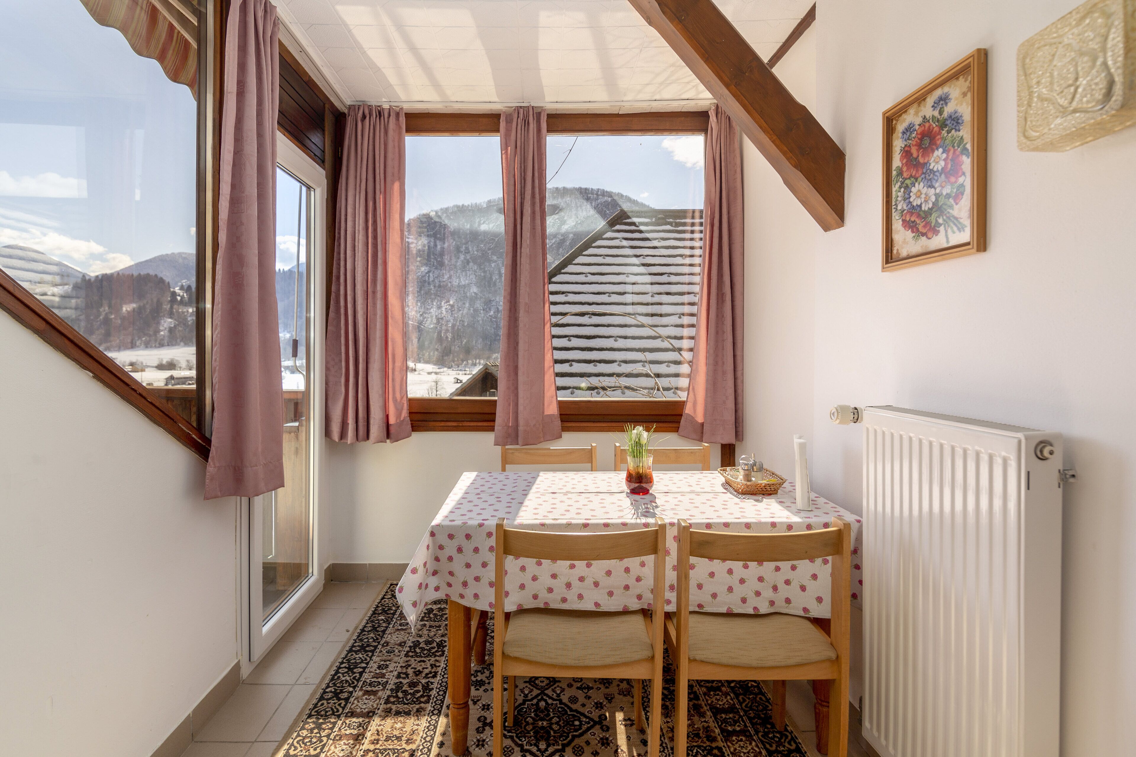 Een eethoek met een tafel voor twee personen, uitzicht op besneeuwde bergen en een radiator aan de muur.