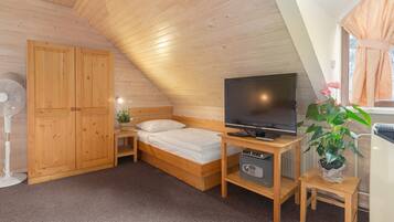 A cozy bedroom with a wooden ceiling, a bed, a TV, a fan, and a potted plant.