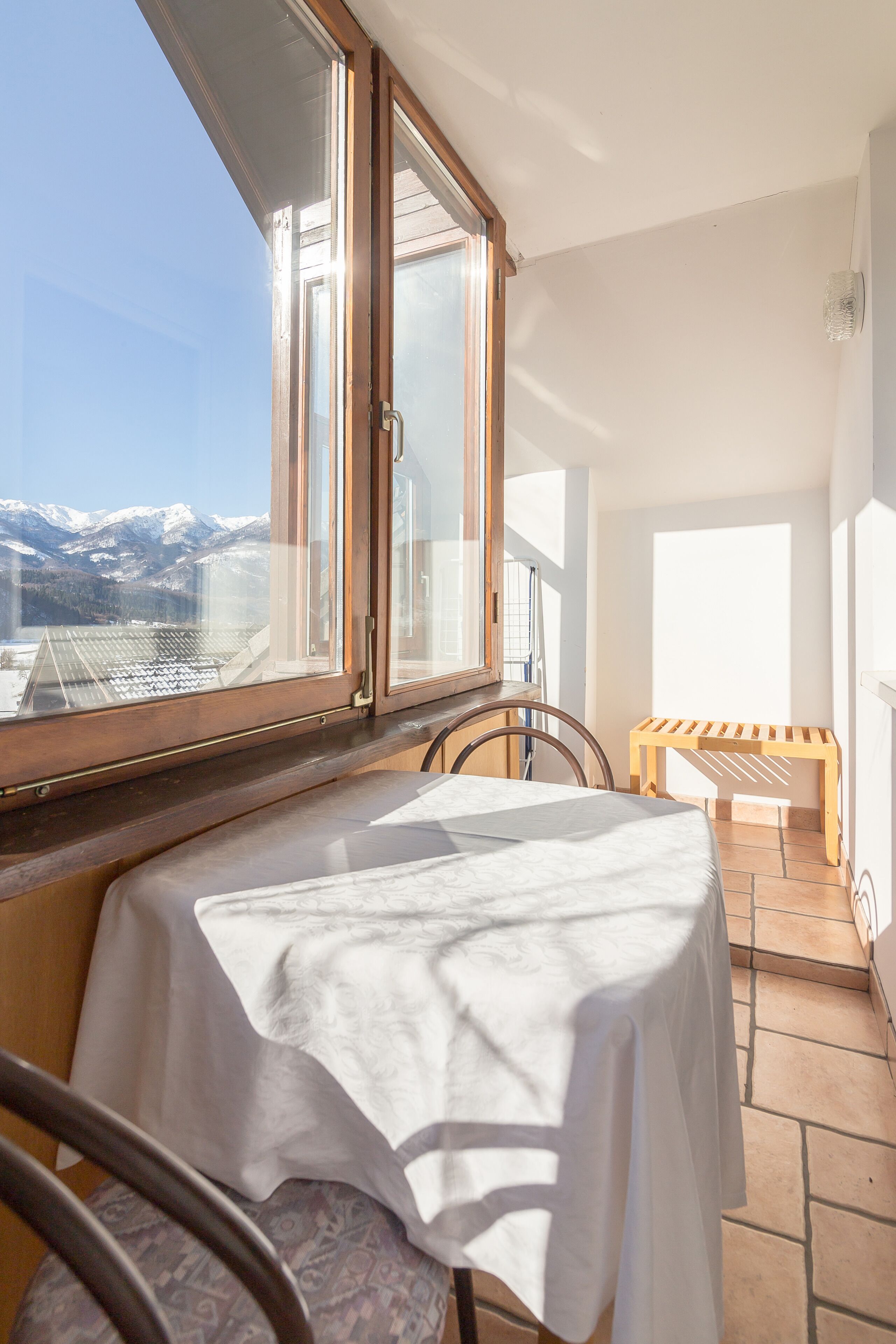 A balcony with a table and chairs, a wooden bench, and a view of snow-capped mountains.