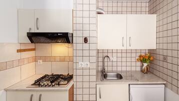 A modern kitchen with a gas stove, white cabinets, a stainless steel sink, and a small refrigerator.
