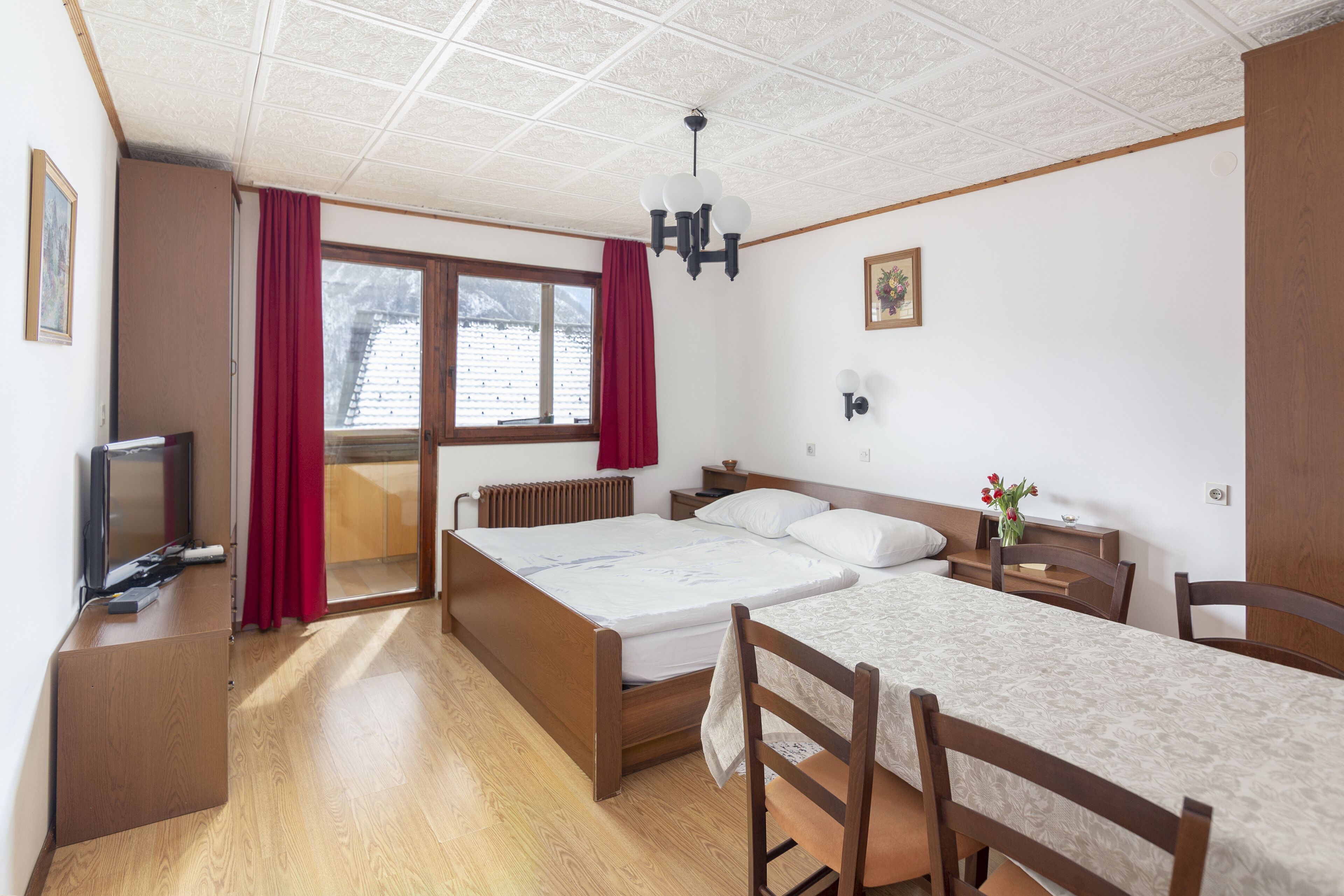 Une chambre à coucher comprenant un lit, un bureau, une chaise, un téléviseur et une fenêtre avec des rideaux.