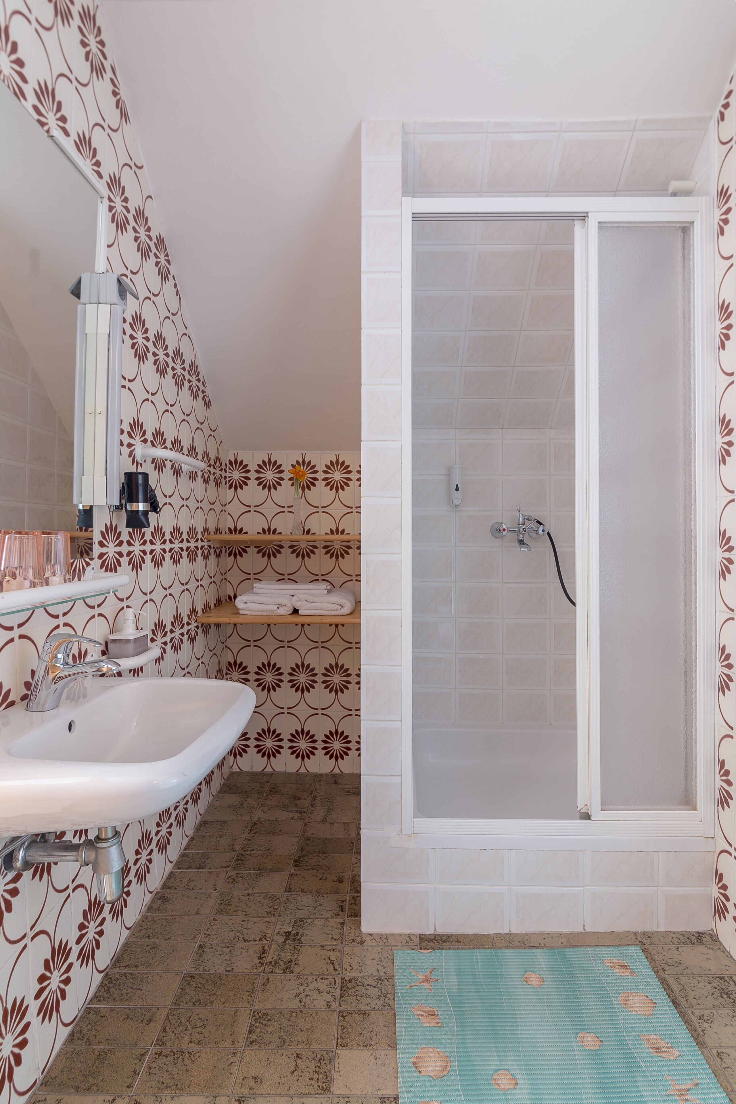 A bathroom with a white sink, a glass shower enclosure, and patterned walls.