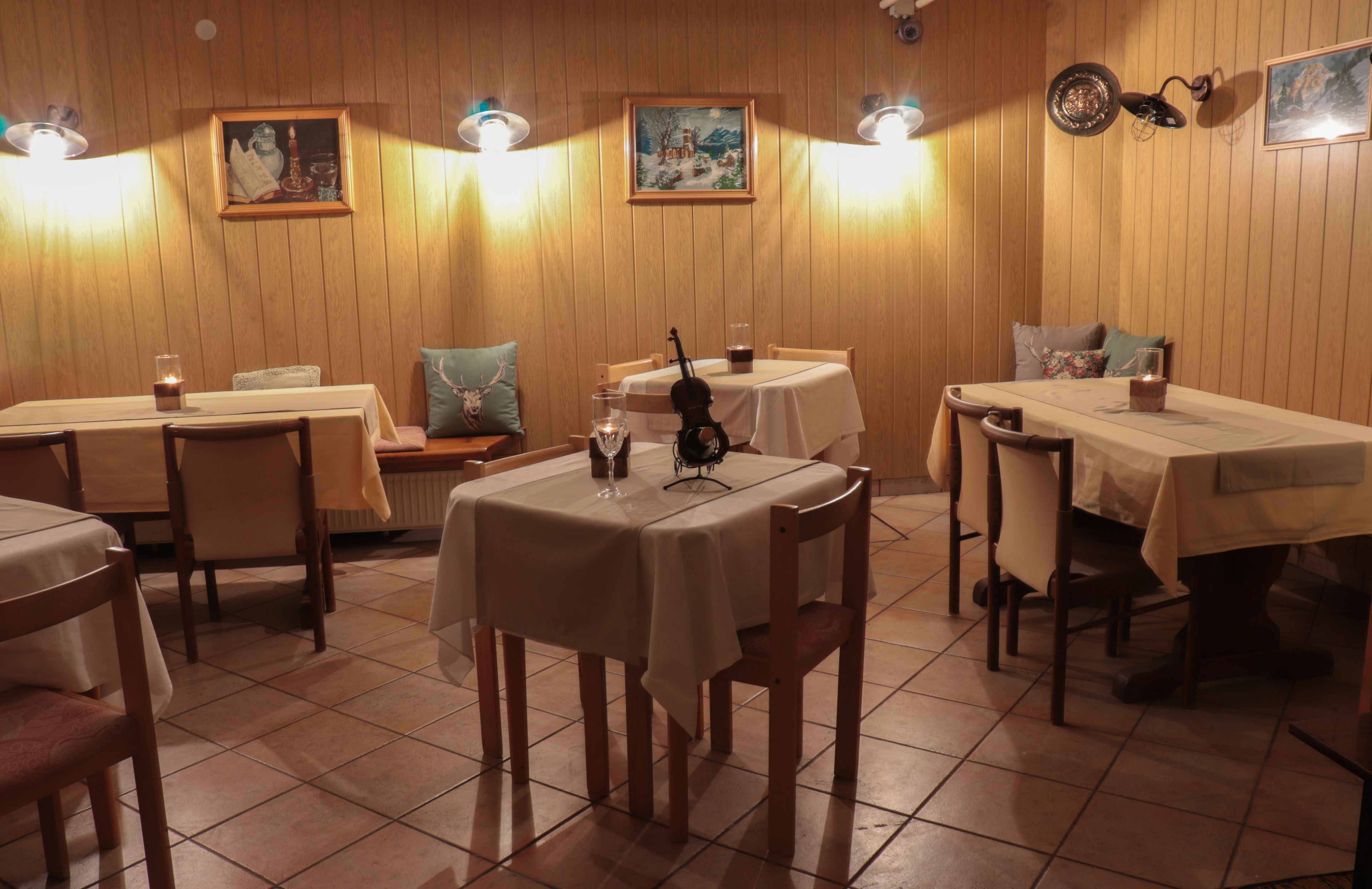 Ein Restaurant mit Holzwandverkleidung, mehreren Tischen mit weißen Tischdecken und einer Geige auf einem Tisch.