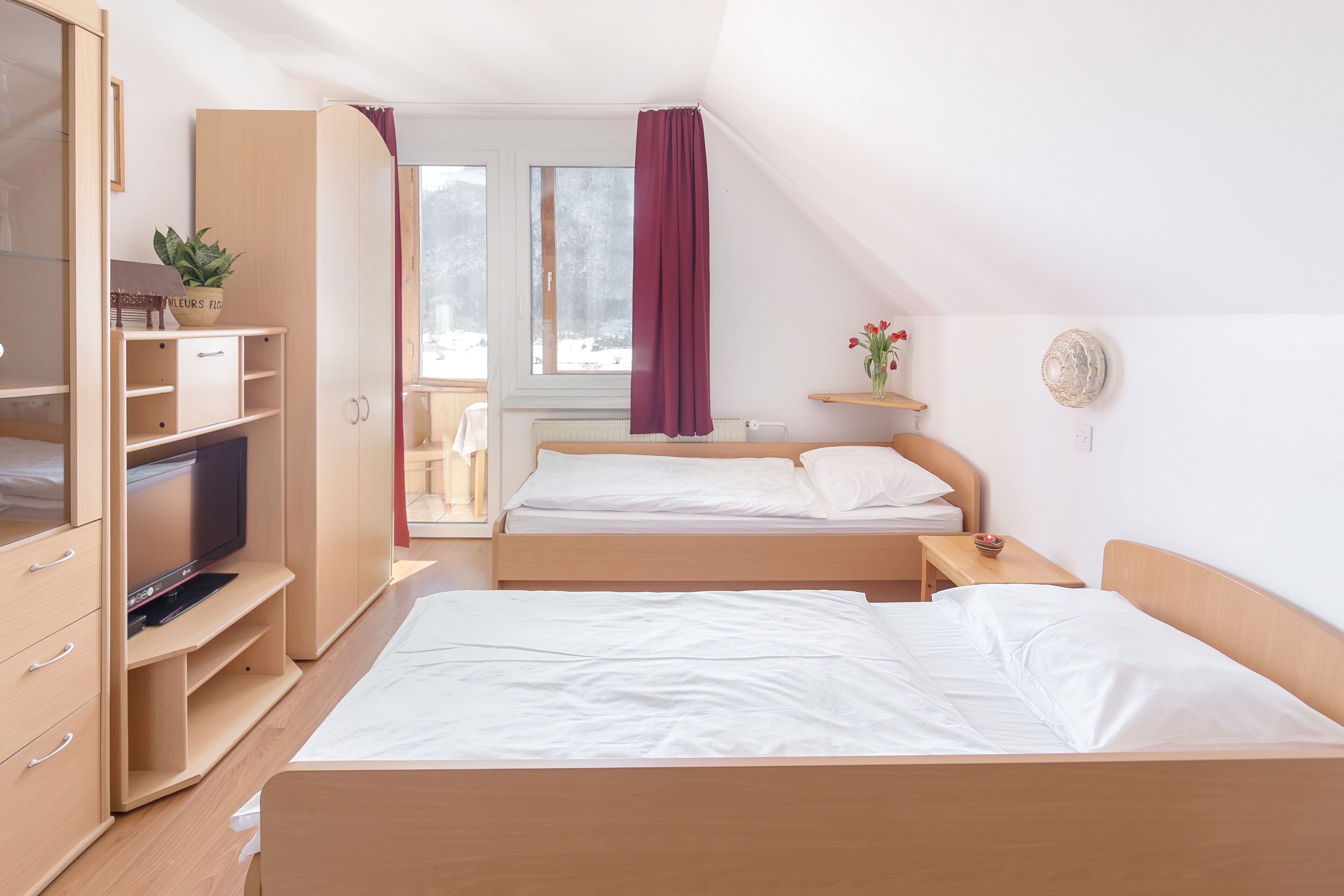 A bedroom with two beds, a TV, a desk, and a window with curtains.
