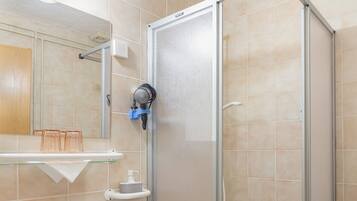 A bathroom with a glass-enclosed shower, a white sink, and a wooden stool.