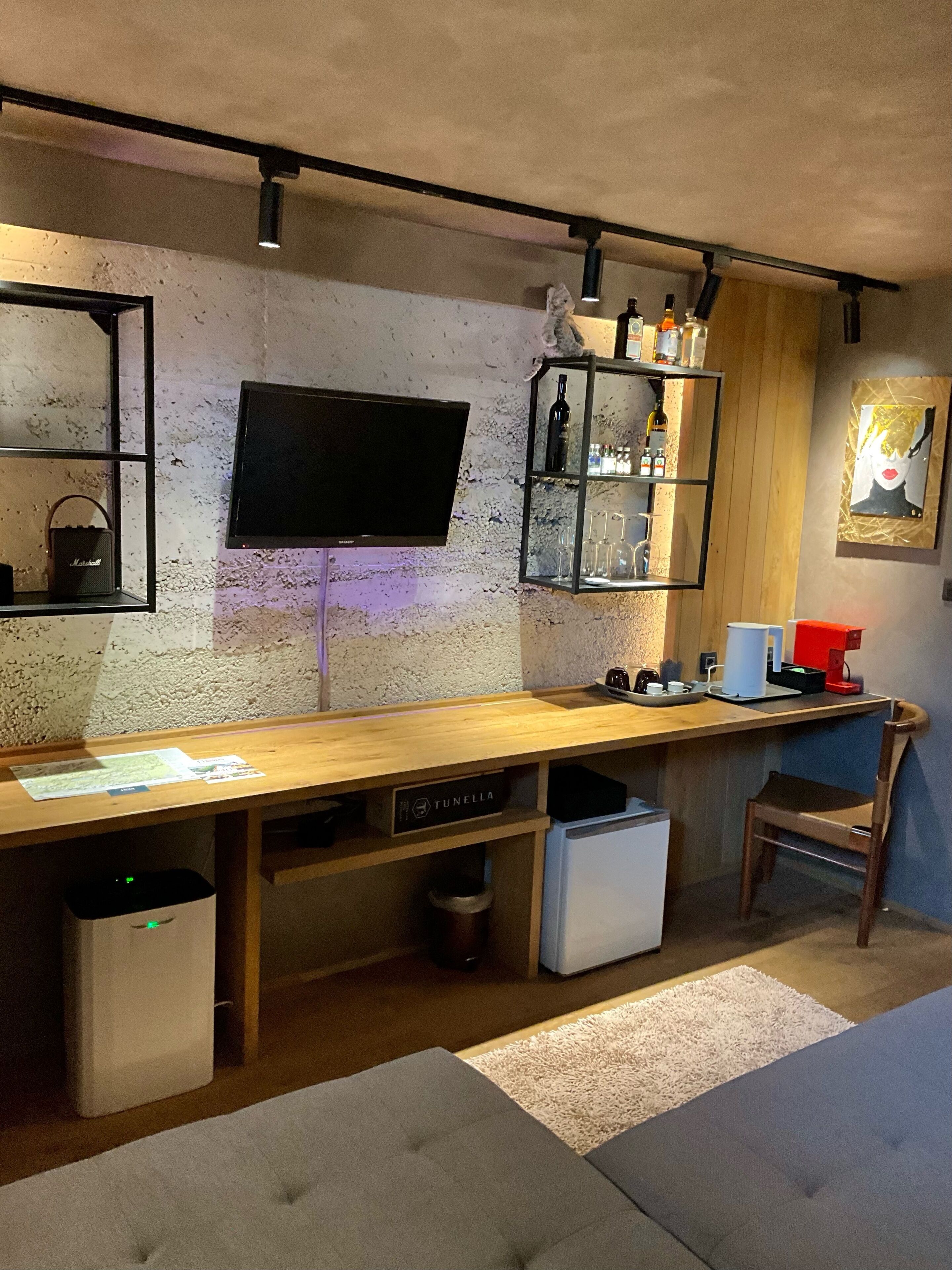 A modern kitchen with a wooden countertop, built-in appliances, a TV mounted on the wall, and a shelf with bottles and glasses.