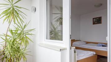 A balcony with a potted plant, a window, and a bed in the adjacent room.
