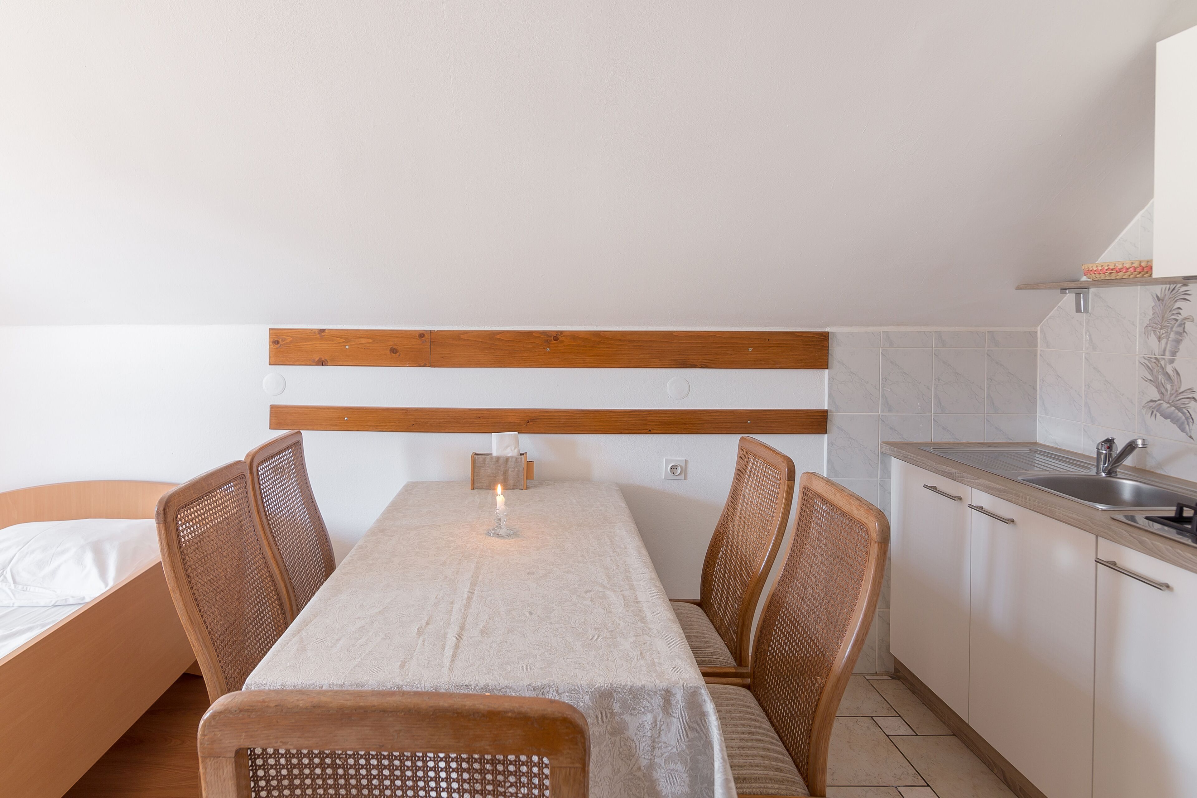 Eine kompakte Küchenzeile mit Spüle und Schränken, ein Essbereich mit Tisch und Stühlen sowie ein Bett mit Holz Kopfteil.