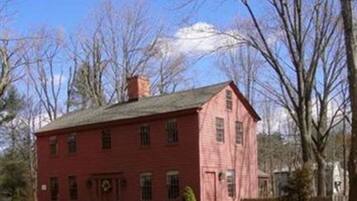 Une maison en bois rouge, avec un toit à pignon, un porche à l’avant et une cheminée.