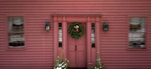 A red building with a central door, two windows on either side, and a wreath above the door. - Green Acres B&B (Simsbury)