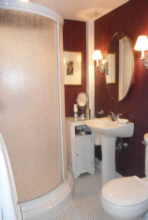 A bathroom with a white toilet, a sink, a mirror, and a shower enclosure. - Green Acres B&B (Simsbury)