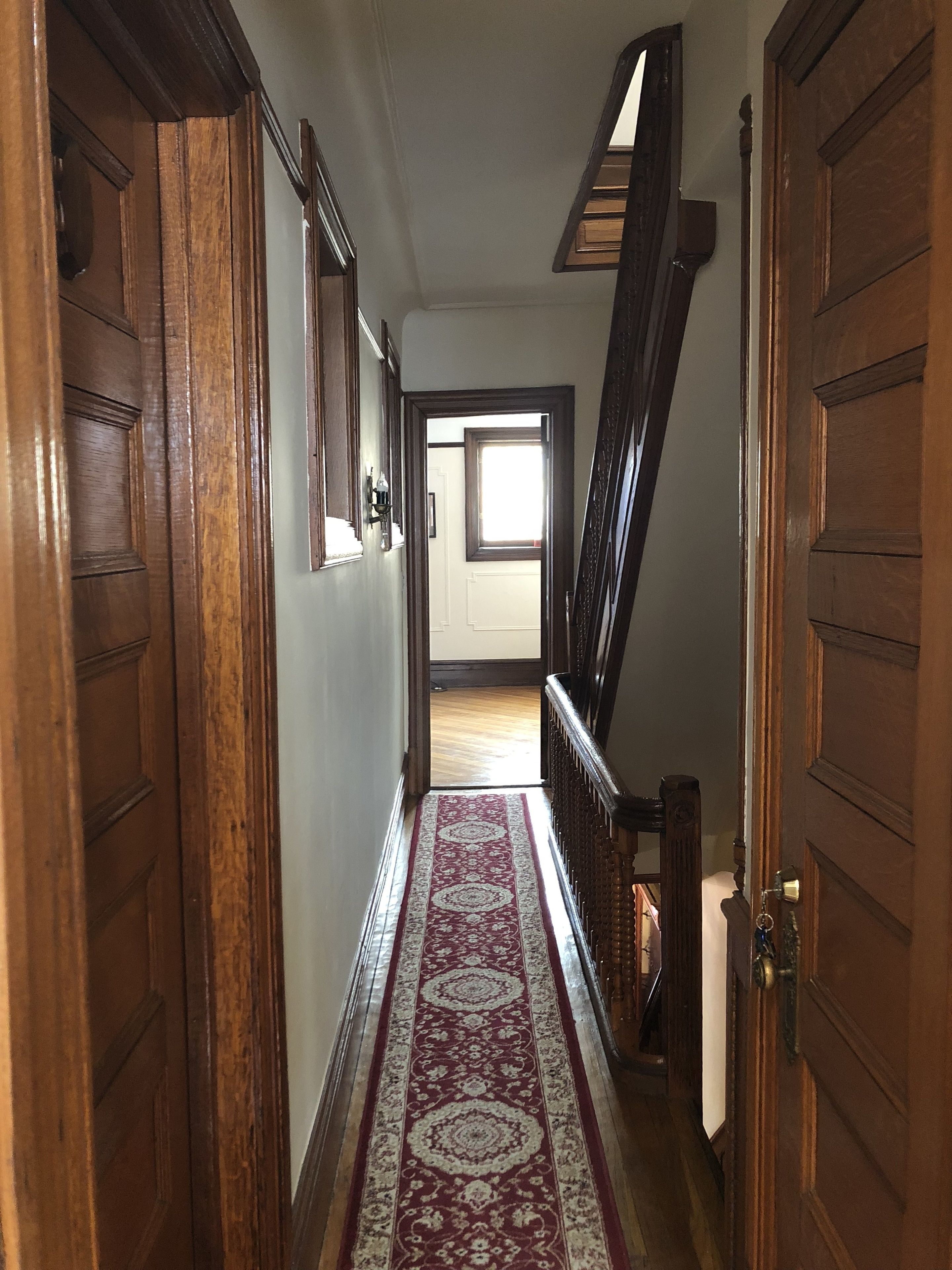 A wooden hallway with a patterned carpet, wooden doors, and a staircase leading to an upper floor.