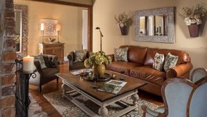 Ein gemütliches Wohnzimmer mit einem braunen Ledersofa, gemusterten Kissen, einem Couchtisch mit Vase und Kerzen sowie einem Kamin, Spiegel und Wandbildern.