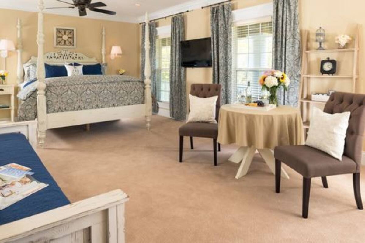 A bedroom with a four-poster bed, a round table with chairs, a television, and a bookshelf.