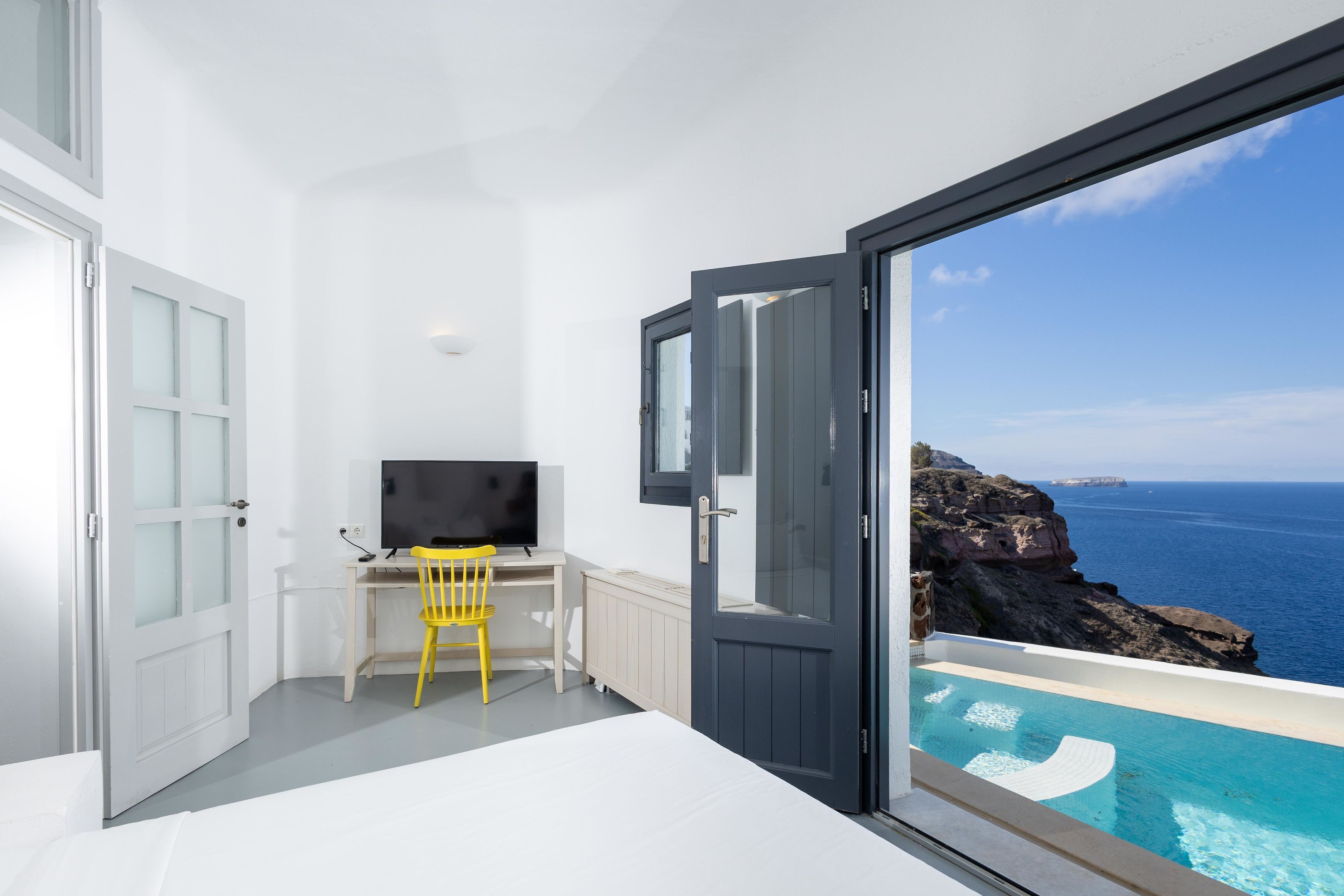 Ein Zimmer mit einem Bett, einem Schreibtisch mit Stuhl, einem Fernseher und einem großen Fenster mit Meerblick.