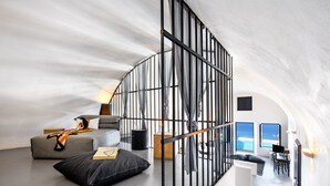 Un interior modern amb un sostre corbat, una escala amb barana metàl·lica, un sofà, un escriptori i vista a l'oceà.