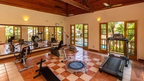 Un gimnasio con diverso equipamiento de ejercicio, ventanas amplias y suelo a cuadros.