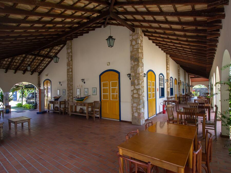 Un amplio patio cubierto con suelo de baldosas, mesas y sillas de madera, y pilares de piedra.
