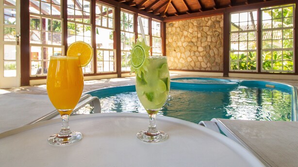 Dos bebidas sobre una mesa cerca de una piscina con un muro de piedra y vigas de madera.