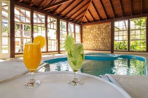 Dos bebidas sobre una mesa cerca de una piscina con un muro de piedra y vigas de madera.