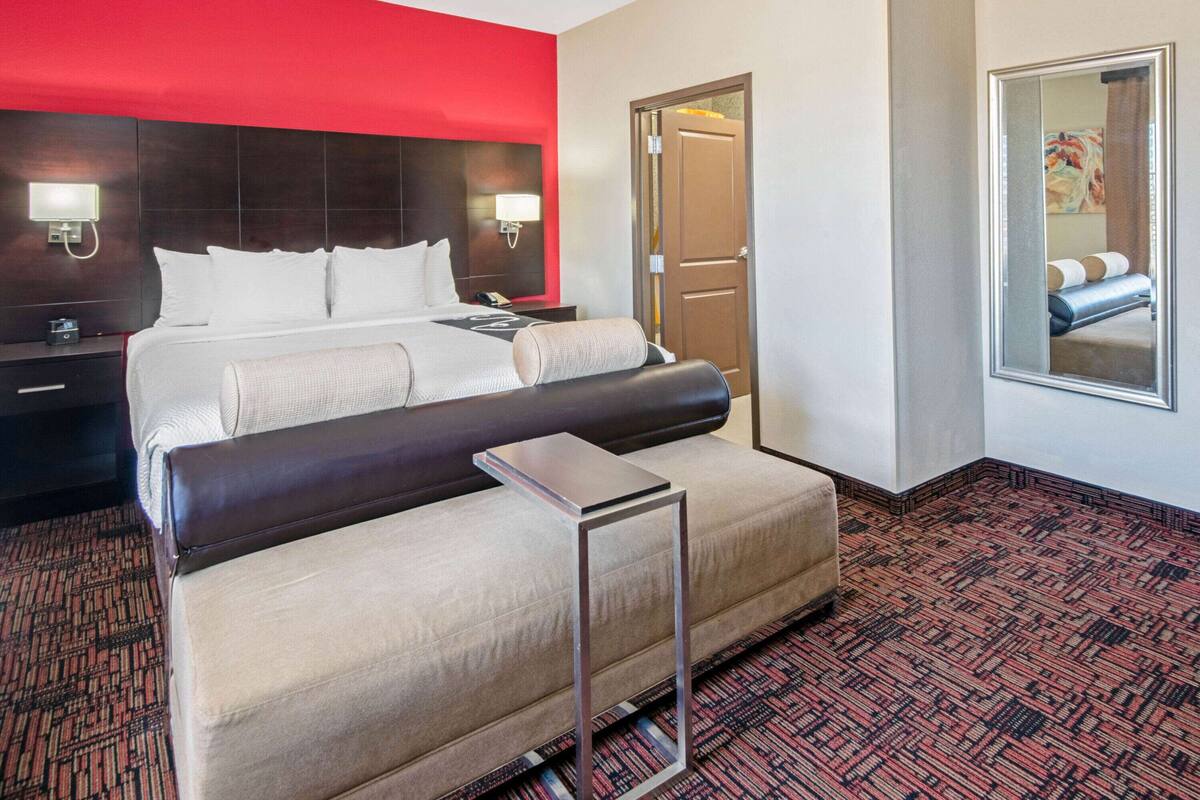 A hotel room with a large bed, a bedside table with a lamp, a small desk, and a mirror on the wall.
