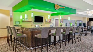 Zona de bar con una pared verde de acento, un televisor y taburetes.