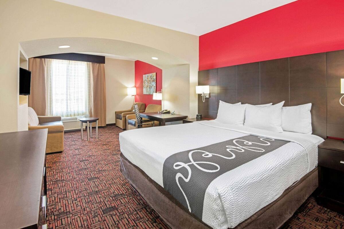 A hotel room with a large bed, a desk, a chair, a TV, and a window with curtains.