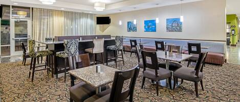 A hotel dining area with patterned carpet, multiple tables and chairs, and artwork on the walls.