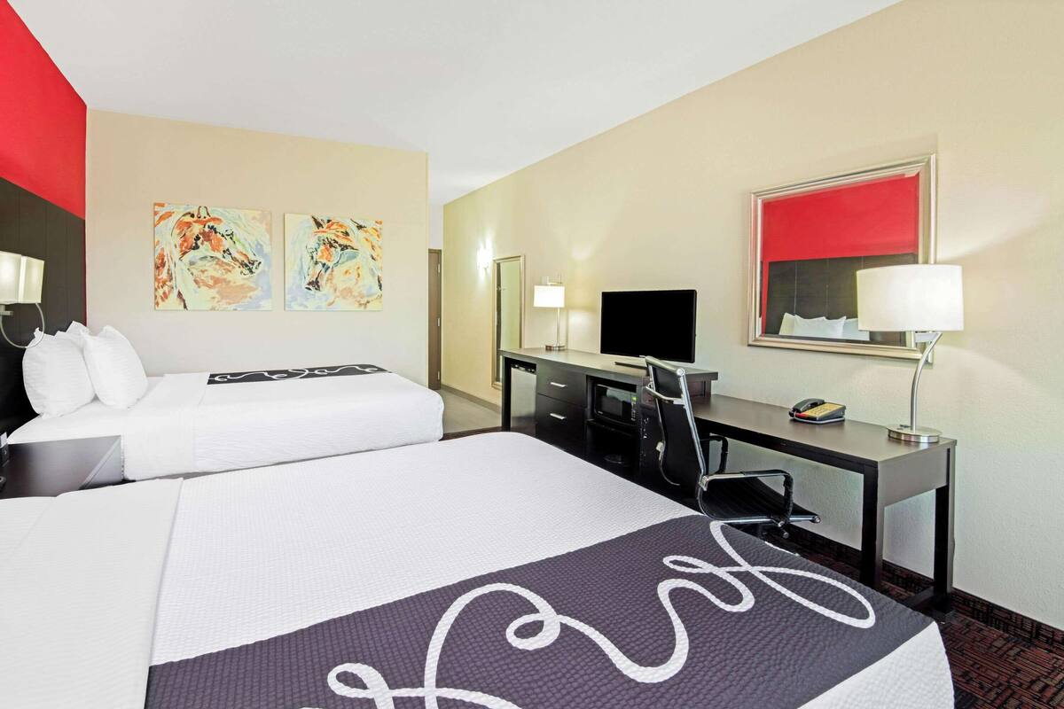 A hotel room with two beds, a desk, a TV, and artwork on the walls.