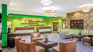 Un vestíbulo de hotel con paredes verdes, una recepción, zona de estar con sofás y sillones, y estanterías decorativas.