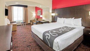 Habitación de hotel con una cama grande, un escritorio, una silla, una mesita, una lámpara y un televisor.