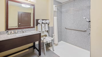 A bathroom with a granite countertop sink, a large mirror, a shower with a glass door, and a towel rack with folded towels.