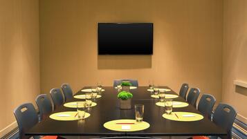 A conference room with a long table, chairs, a flat-screen TV on the wall, and a small plant centerpiece.