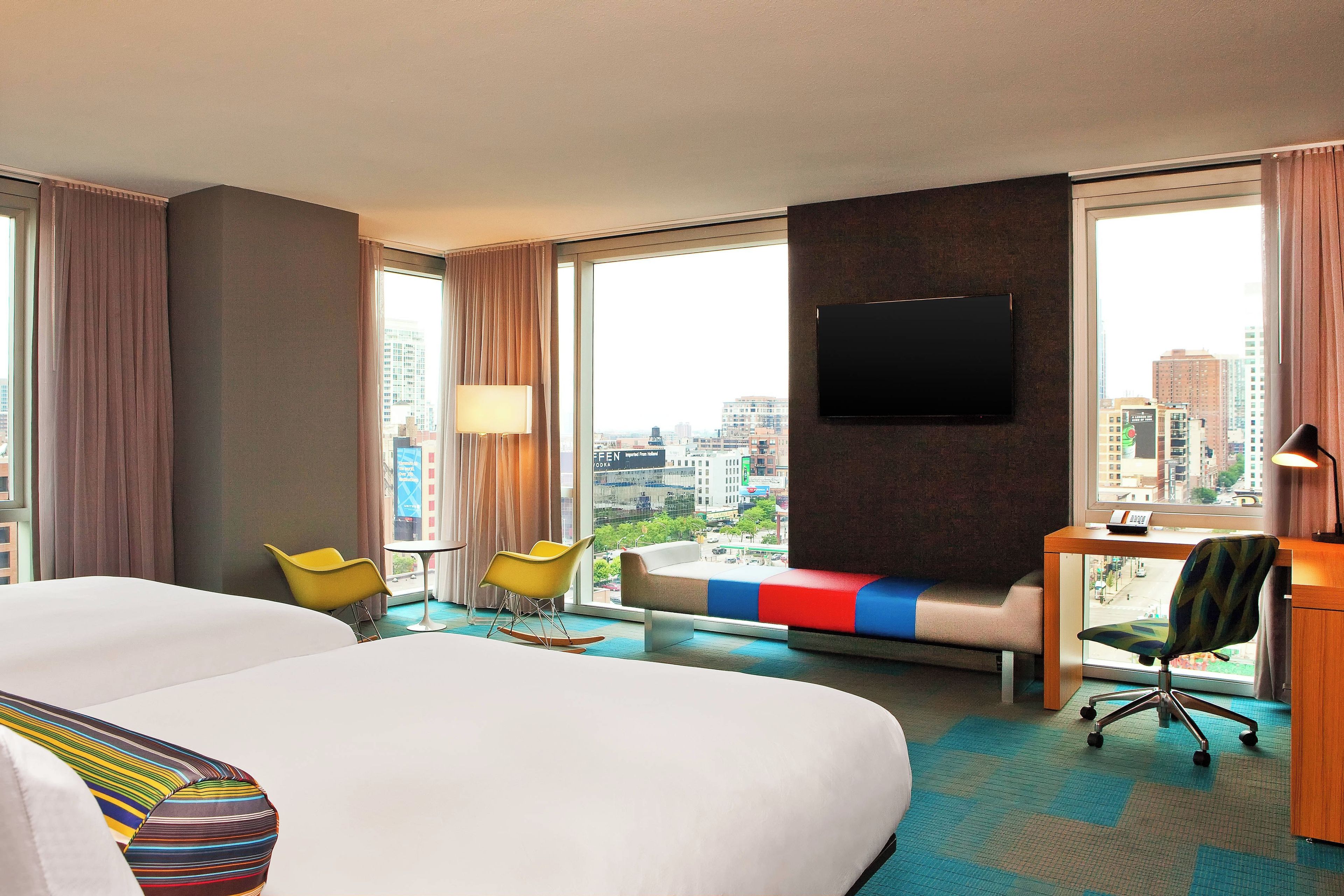 Habitación de hotel con una cama grande, un escritorio, dos sillas, un televisor y vistas a la ciudad.