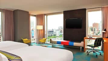Habitación de hotel con una cama grande, un escritorio, dos sillas, un televisor y vistas a la ciudad.
