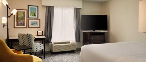 A hotel room with a bed, a desk, a chair, a television, and framed pictures on the wall.