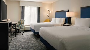 Une chambre d’hôtel avec deux lits, un bureau, une chaise, une lampe et un téléviseur.