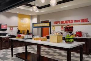 A breakfast area with a counter, a waffle station, and a sign that says 'HAPPY BREAKFAST STARTS HERE.' - Hampton Inn Thomson (Thomson)