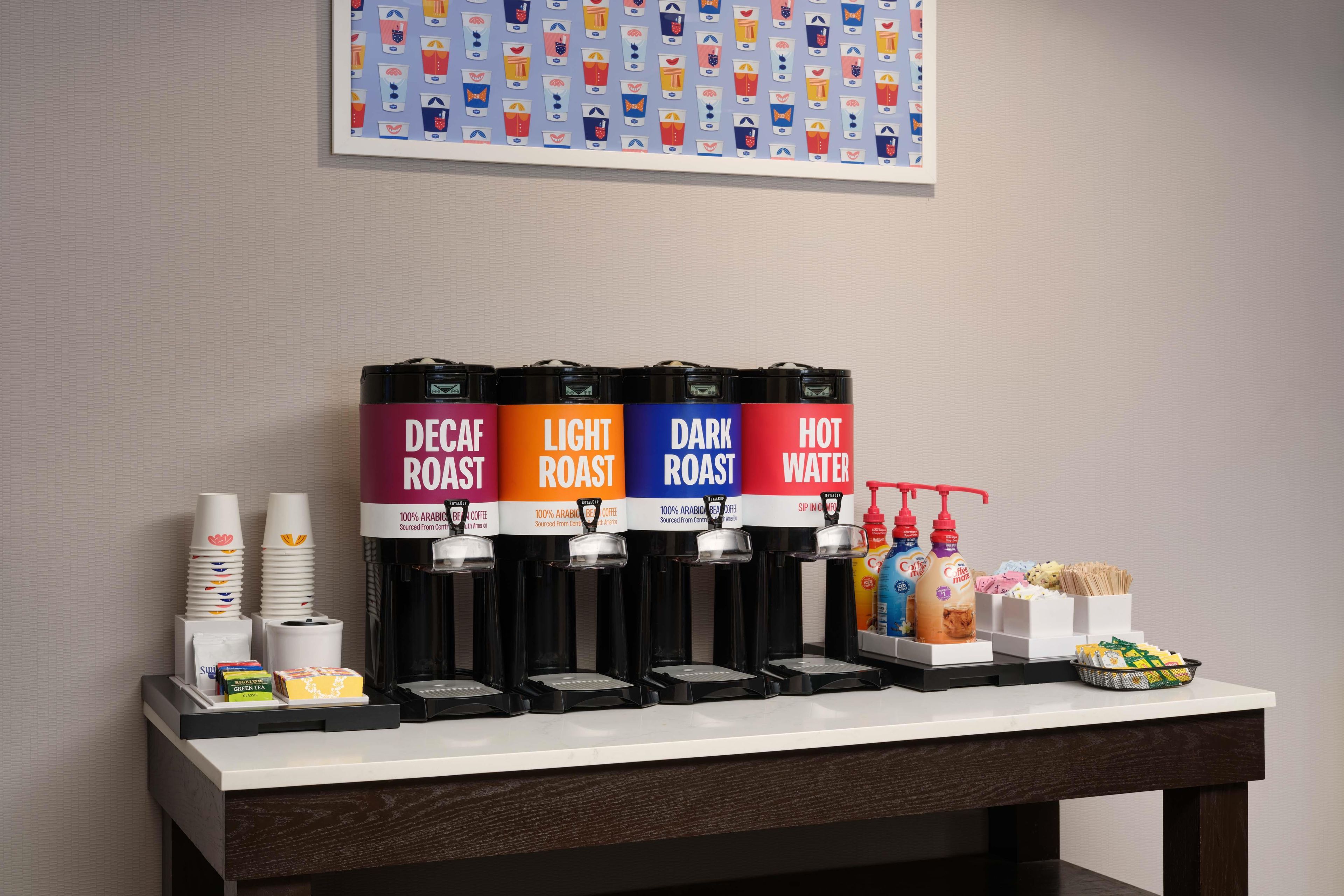 Estación de café con dispensadores etiquetados para café descafeinado, café claro, café oscuro y agua caliente.