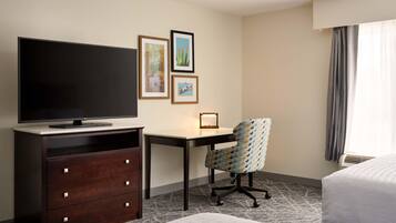 Habitación de hotel con cama, escritorio, televisor, sillón y cuadros en la pared.