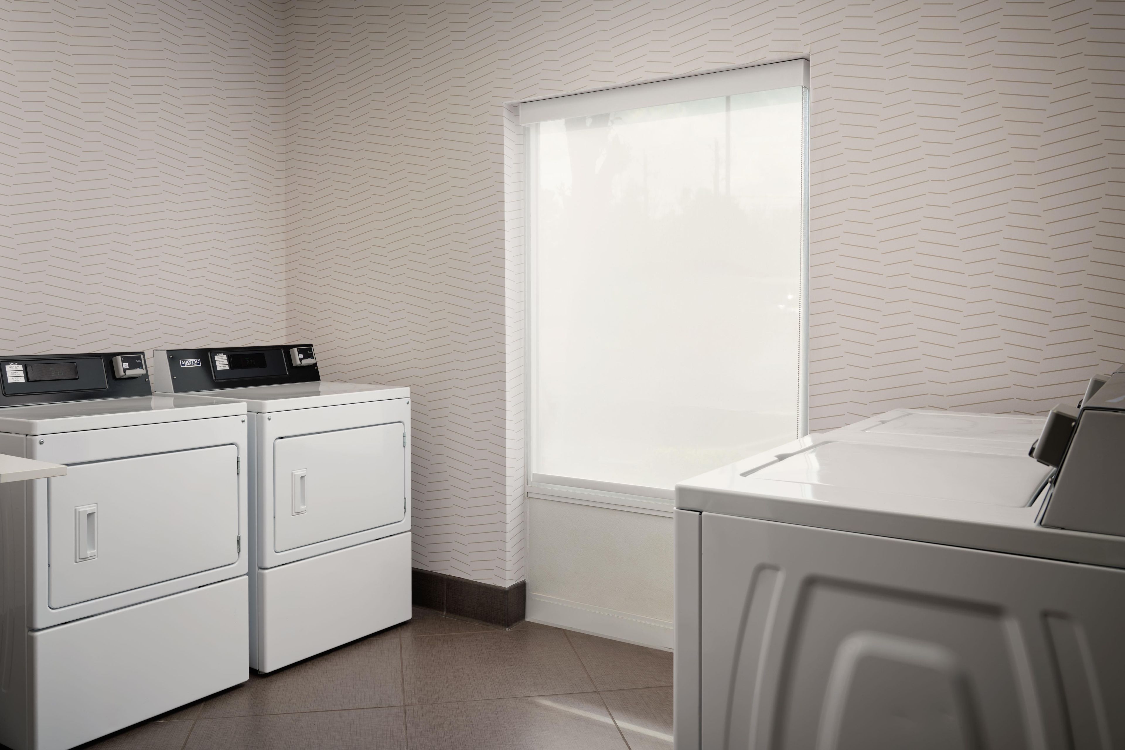 A laundry room with stacked washers and dryers, a window, and a patterned wall.