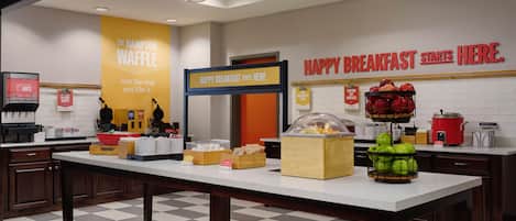 A breakfast area with a counter, a waffle station, and a sign that says 'HAPPY BREAKFAST STARTS HERE.'
